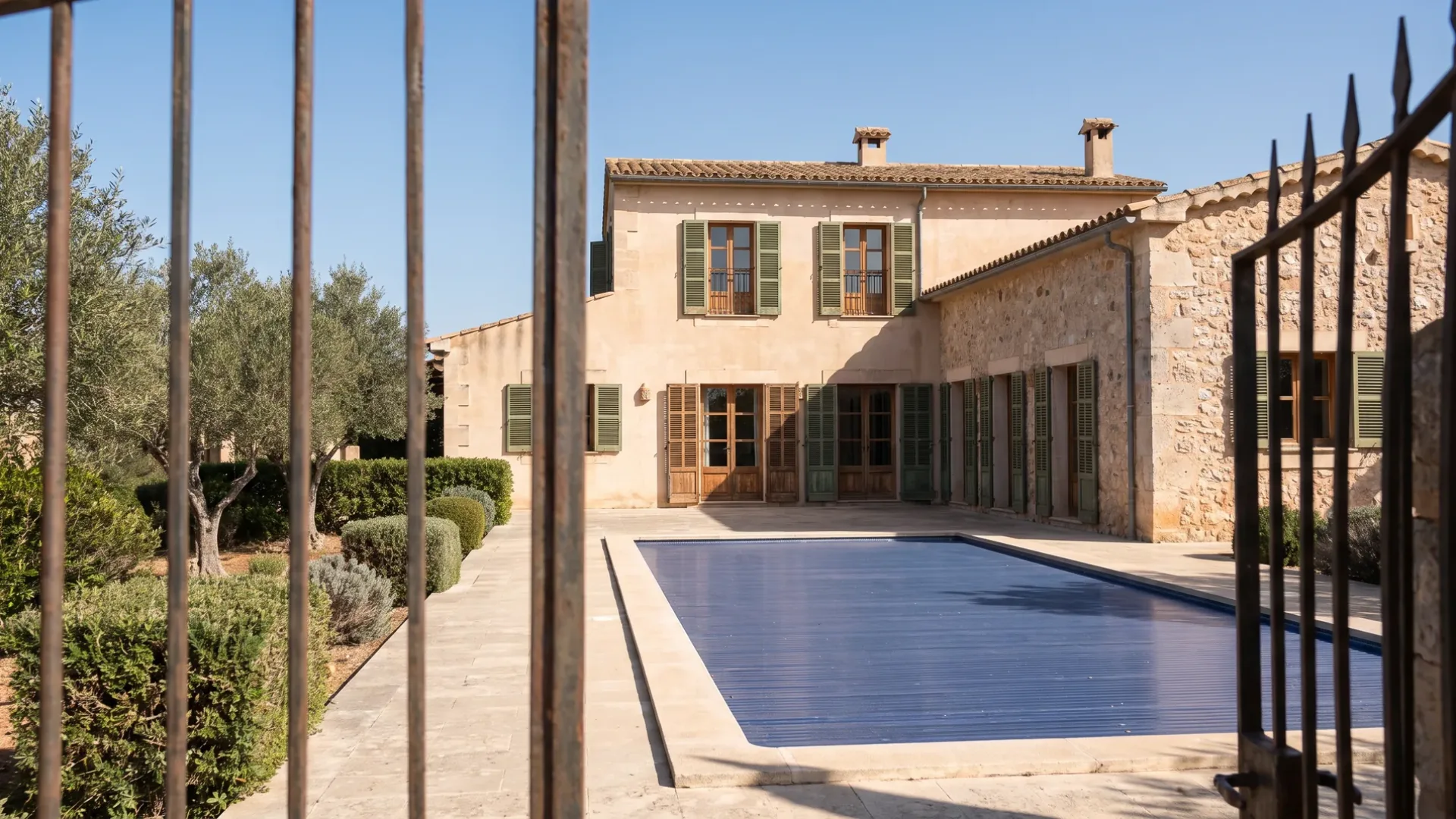 Closed Mallorcan villa seen from its gate with latched shutters and a cover over the pool