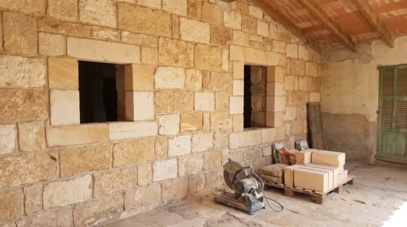 Sandstone wall in a Mallorcan house with weathered blocks cut out and new stone pieced in