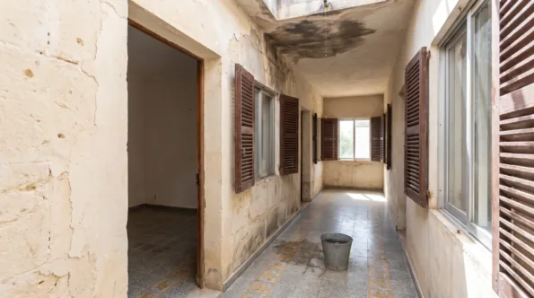 Cellular interior of a concrete-framed Mallorcan villa with dated tiles and a stained ceiling