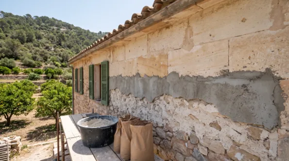 Hard cement render cut off a stone wall in a green Mallorcan valley to expose the stone under it