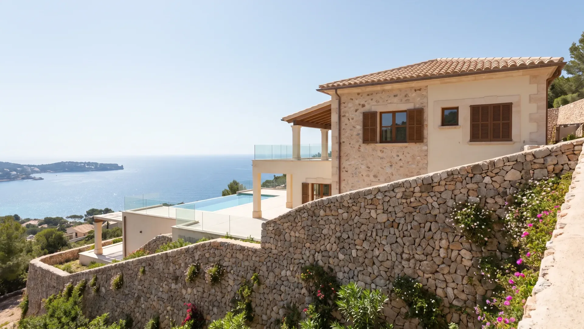 Villa på en brant tomt som hålls av höga planterade stödmurar av sten, en poolterrass nedanför huset och en vik bortom