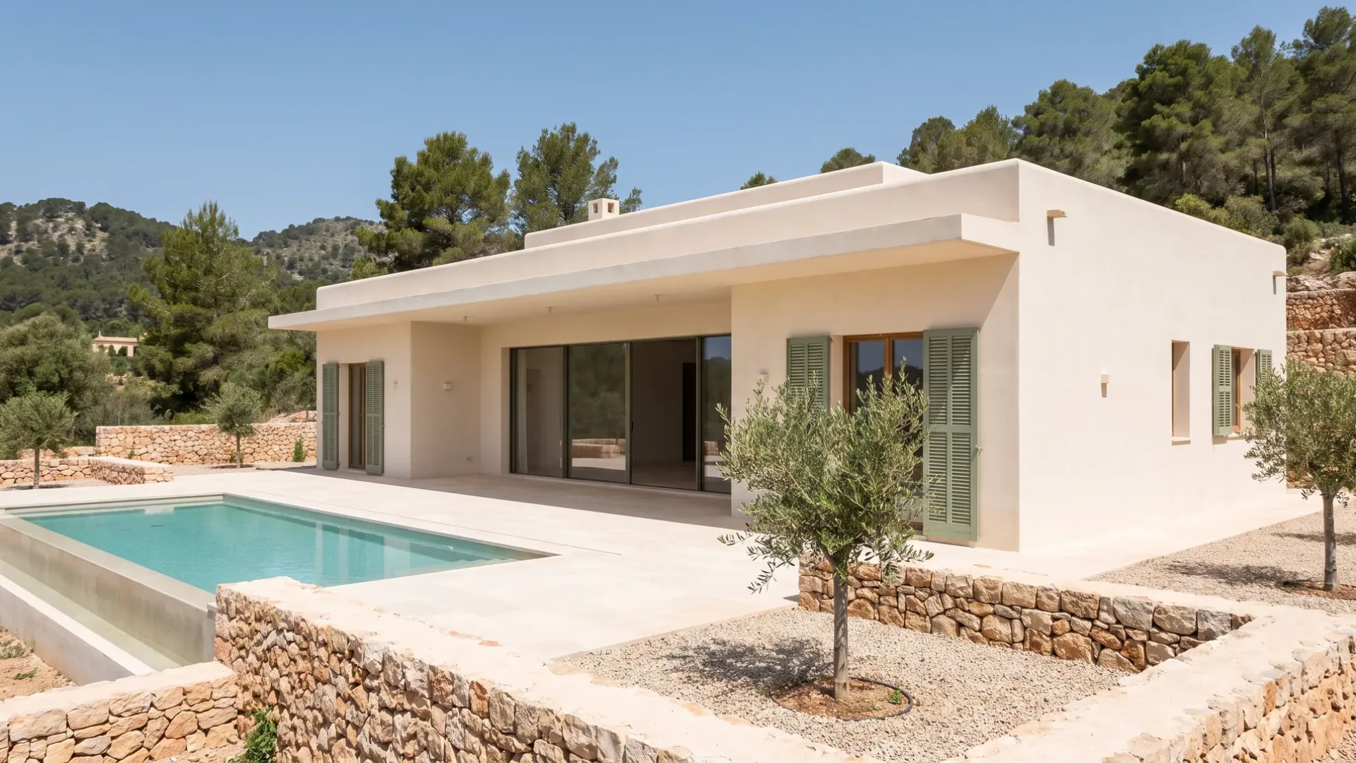 New flat-roofed villa in off-white render with a pool, a limestone terrace, young olive trees and pine-covered hills