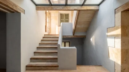 Stairwell with stone steps and timber treads under a glazed rooflight, lime-plastered walls and a terracotta landing
