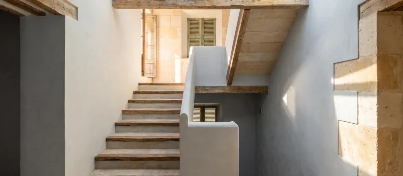 Stairwell with stone steps and timber treads under a glazed rooflight, lime-plastered walls and a terracotta landing
